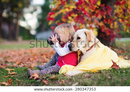 A portrait of a cute little girl drinking tea from a mug and sitting next to her dog, a yellow labrador wrapped up in a warm blanket