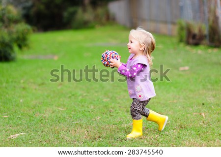 A cute little toddler girl holding a pet toy- a colorful rope ball in the park on a cool summer or autumn day