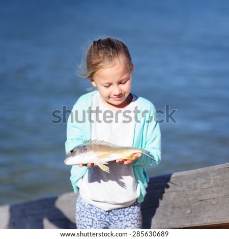 A cute little girl holding a fish with the sea water in the background, focus on the fish