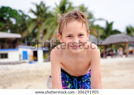 A close up portrait of a happy boy wearing swimming shorts at the beach smiling into the camera