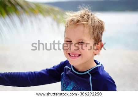 A portrait of a happy boy with a crooked tooth wearing lycra sun protective top at the beach smiling into the camera