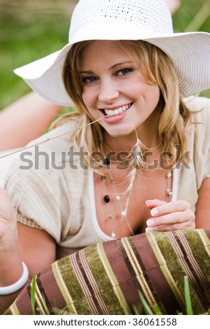 Woman lying in the grass with a pillow, holding a piece of wild grass in her mouth