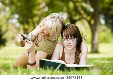 Cheerful woman using cellphone while her friend reads a book