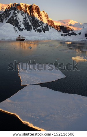 Midnight sun on the mountains above a tourist boat in the Lamaire Channel on the Antarctic Peninsula in Antarctica.