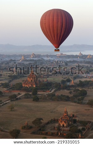 Hot air balloon flying over the temples of the Archaeological Zone in Bagan in the early morning sunlight. In the distance is the Irrawaddy River. Myanmar (Burma).