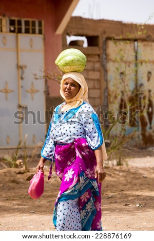 TATA, MOROCCO, AUGUST 30: Unidentifed Moroccan woman carrying a watermelon on her head in the city of Tata and wearing the traditional Moroccan clothes. Morocco 2014.