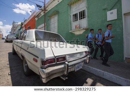 CIUDAD BOLIVAR, VENEZUELA, APRIL 9: Old wreck car parked in the old colonial city of Ciudad Bolivar with kids walking back from the school dressed in their blue uniform. Venezuela. April 9, 2015.