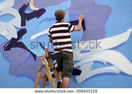 BERLIN, GERMANY, JULY 8: Unidentified painter in action on the wall of Berlin, painting a blue graffiti. Germany 2008