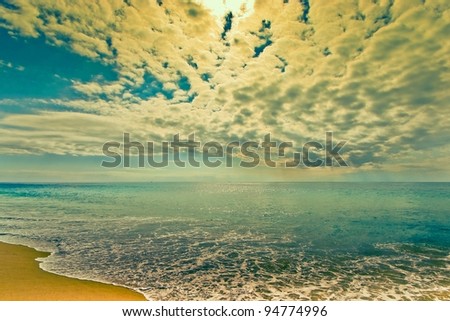 Waves rolling on tropical shoreline with Late-afternoon summer sun, streaming clouds and blue sky.