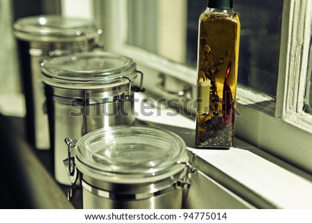 Stainless steel storage containers and bottle of olive oil in kitchen on windowsill shelf in warm sunlight.