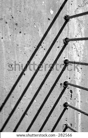 Detail of high tension steel cables protection railing embedded in concrete with diagonal shadows