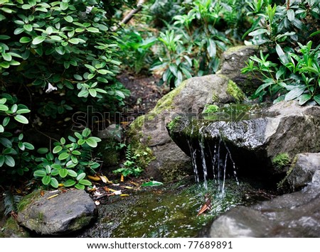 Gentle stream and waterfall features with stones and boulders in a Nature park and landscaped garden grounds in springtime