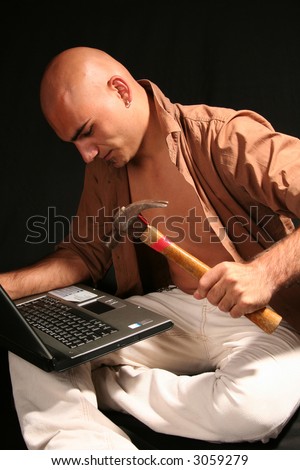 Furious young man destroying  laptop with a hammer