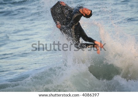 Young man in sea on boogie board jumping a wave