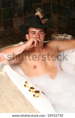 sexy muscular young man in a bubble bath spa with a hat and cigar