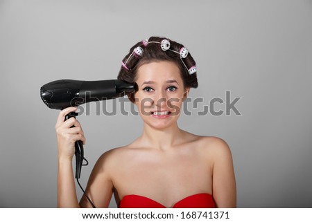 Girl holding a hair dryer as a gun at light background