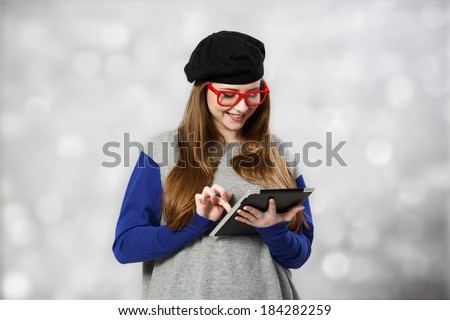 Girl at glasses and beret works with tablet pc at light background