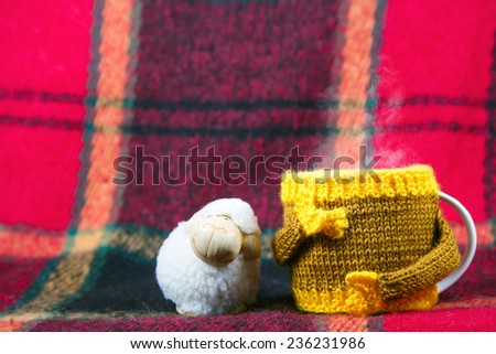 Knitted  yellow cup and sheep  at red rug background