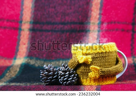 Knitted  yellow cup and cones at red rug background