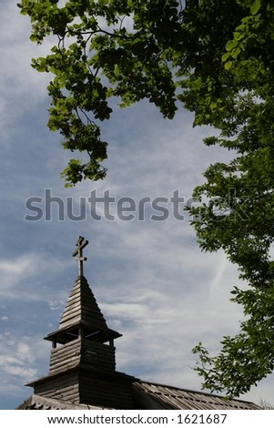 Tower of Russian wooden chapel framed by green leafage
