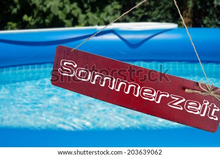 Swimming pool in a garden and sign with the german word Summer time / Summer Time
