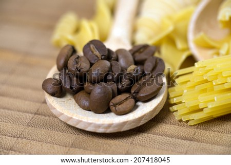 Wooden spoon with pasta and coffee beans on a wooden board / pasta with coffee beans