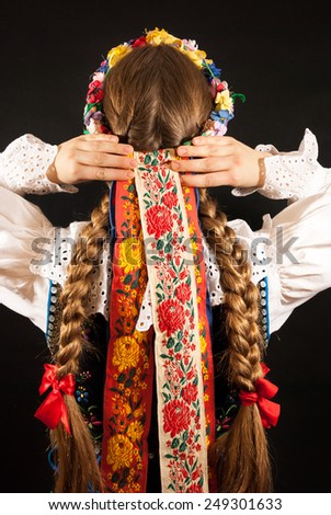 A young woman with long blonde hair tresses wearing a traditional Polish folk costume on a black background