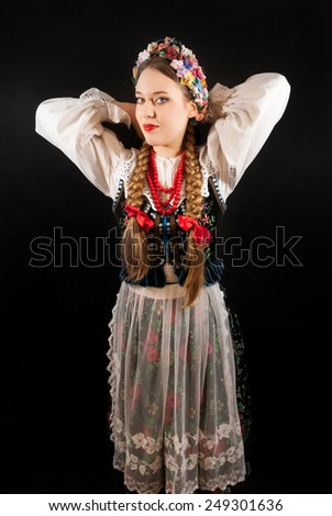 A young beautiful woman with long blonde hair tresses wearing a traditional Polish folk costume on a black background