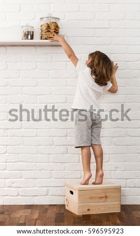 Cute little boy reaching for the chocolate chip cookies on the kitchen shelf