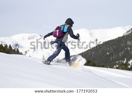 Young man running along the side of a snowy mountain with snowshoes