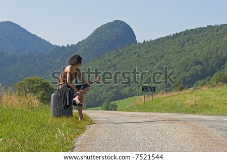 Woman sitting on her suitcase making of hitch-hiking