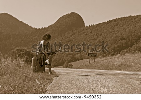 Woman sitting on her suitcase making of hitch-hiking