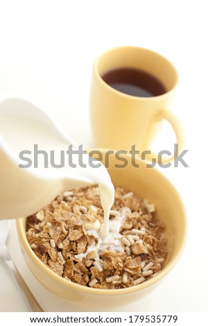 Pouring milk from a ceramic jug into a bowl of nutritional breakfast cereal or muesli with a freshly brewed mug of espresso coffee alongside