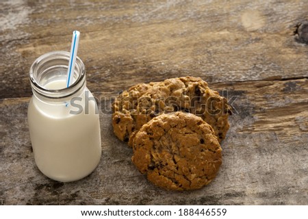 Milk and cookies childhood treat set out on an old rustic wooden table with a glass bottle of fresh milk with a straw and a pile of crunchy cookies, high angle with copyspace