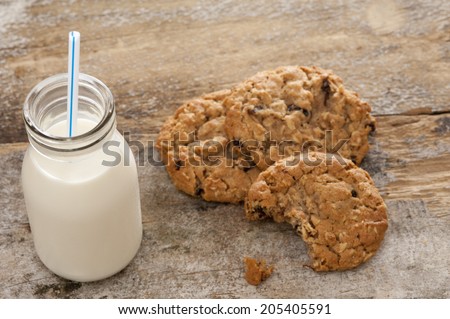 Small glass bottle of fresh creamy farm milk with a straw alongside half eaten crunchy cookies on a rustic wooden surface, high angle view