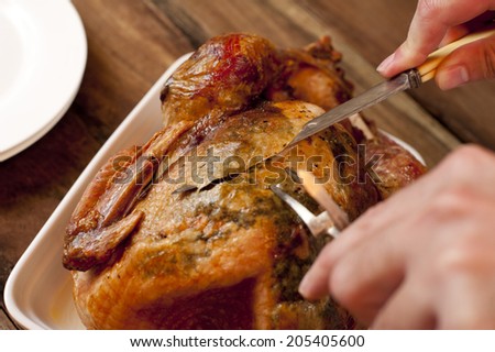 Close up view of the hands and utensils from above of a man carving a delicious brown roast chicken for dinner
