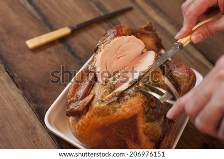 Overhead view of the hands of a man carving a roast turkey with a carving knife and fork slicing the breast meat ready for a Thanksgiving or Christmas dinner