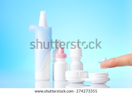 contact lens on finger  and eye drops on blue background
