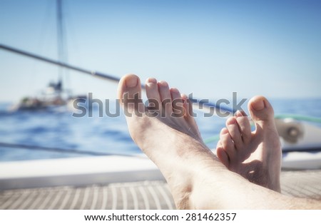 man lounging on a catamaran sailboat trampoline with her feet propped up and crossed.