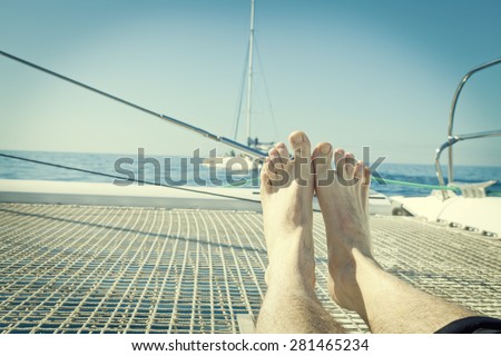 man lounging on a catamaran sailboat trampoline with her feet propped up and crossed.