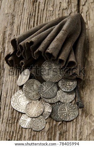 Ancient English silver coins spilling out of a leather purse on an oak table