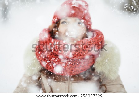 young woman with red scarf playing with snow, selective focus on the snowflakes