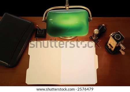 desktop with lamp, pen, briefcase, stapler, pencil sharpener and an open manila file folder with a blank letter-sized sheet of paper