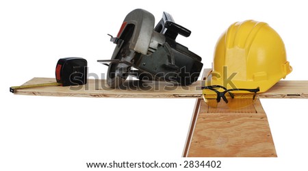 tape measure, power saw, hard hat and wooden plank resting on a saw horse