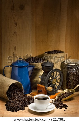 Coffee cup and saucer against a rustic background of burlap bags, coffee beans, coffee grinder, coffee pot and coffee scoop with empty space above for company logo and text