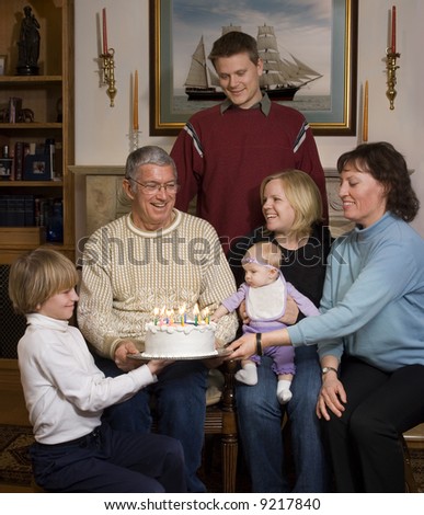 Grandfather receiving birthday cake with grandmother, children and grandchildren