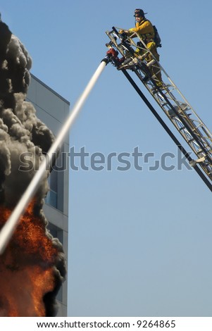 A Fire Man on a lift up high hosing a fire below him