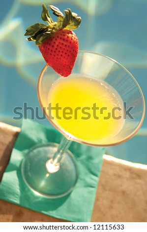 Mango martini shot at pool\'s edge with strawberry from above