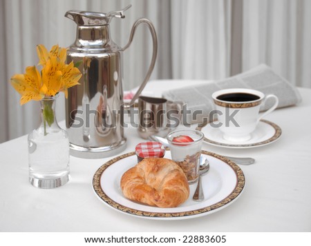 Continental breakfast with a croissant, yogurt and coffee on a white linen tablecloth