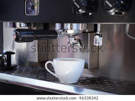 Coffee cup filled with cappuccino coffee, sitting on the tray of a commercial espresso machine